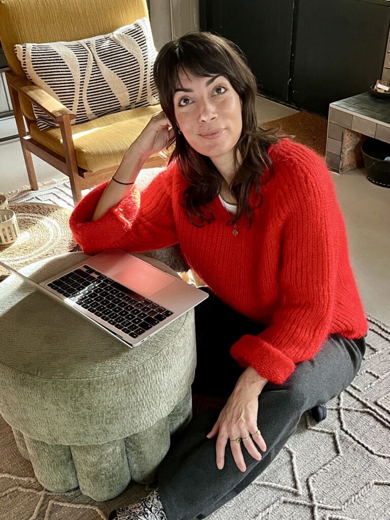 Daphne Maierna in a red jumper, sitting on the floor next to a laptop